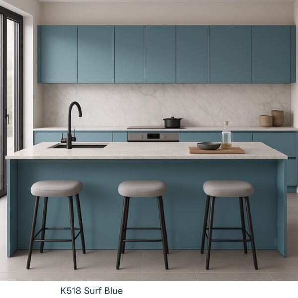 Moderne Einbauküche mit Kücheninsel in der Dekorfarbe K518 Surf Blue, ausgestattet mit matten, grifflosen Fronten, weißer Marmor-Arbeitsplatte, schwarzer Spüle und drei Barhockern vor einem großen Fenster.